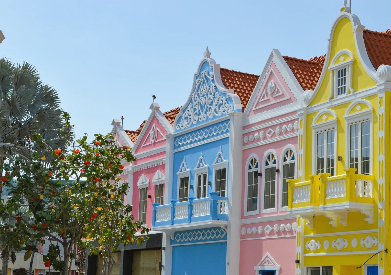 A row of pastel Dutch-gabled houses in pink blue yellow and white on a sunny street.