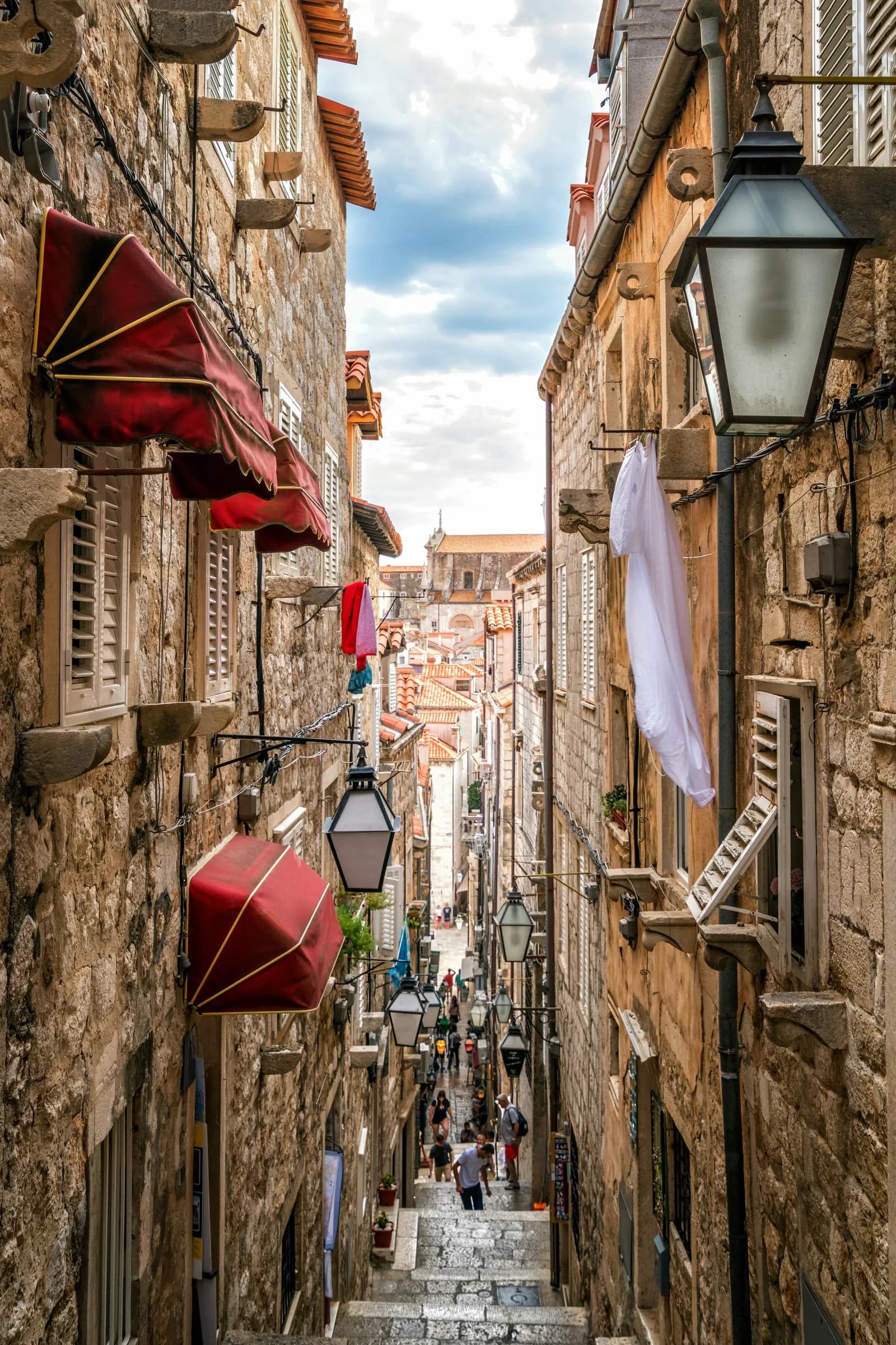A narrow staircase street between tall stone houses with red lanterns and white laundry hanging out.