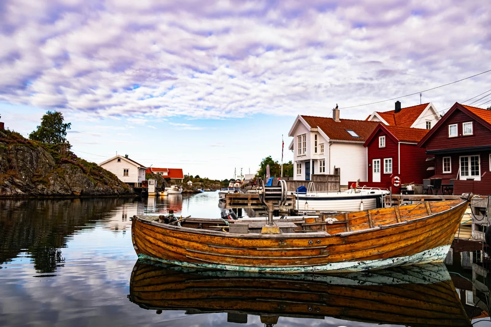 A wooden rowing boat moored on a calm inlet among the red-and-white timber houses of the southern Norwegian coast.