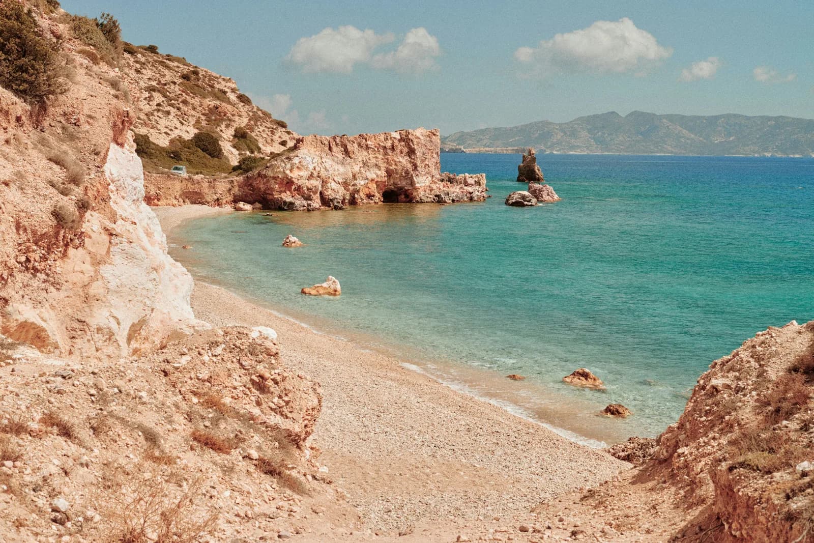 Pale rock cliffs around a small pebble cove on a Cycladic island