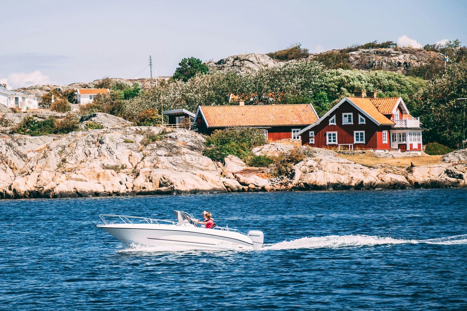 A small motorboat crossing blue water past red wooden sea cabins in the Strömstad archipelago.