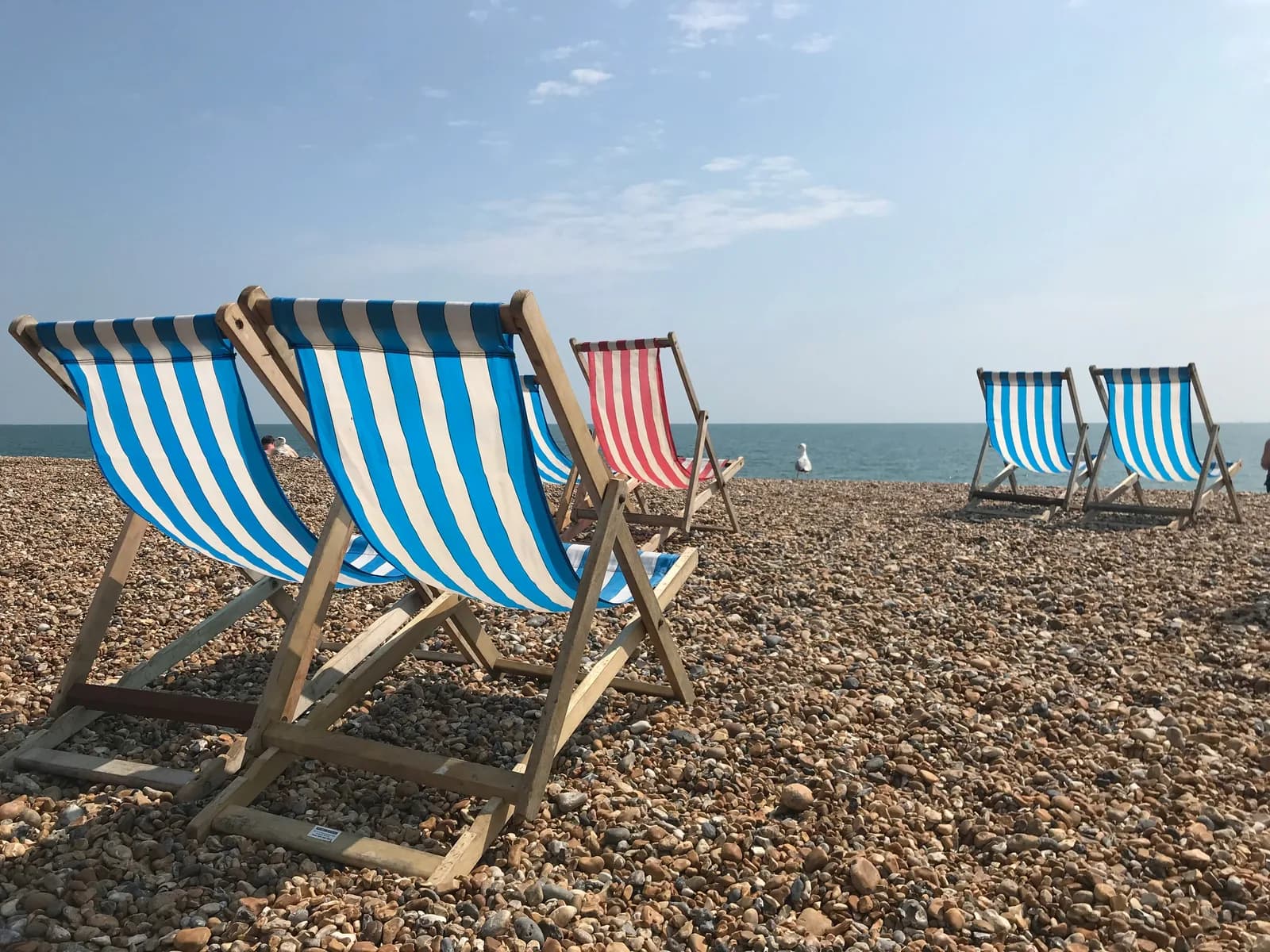 Striped blue and red deckchairs on a pebble beach with calm sea
