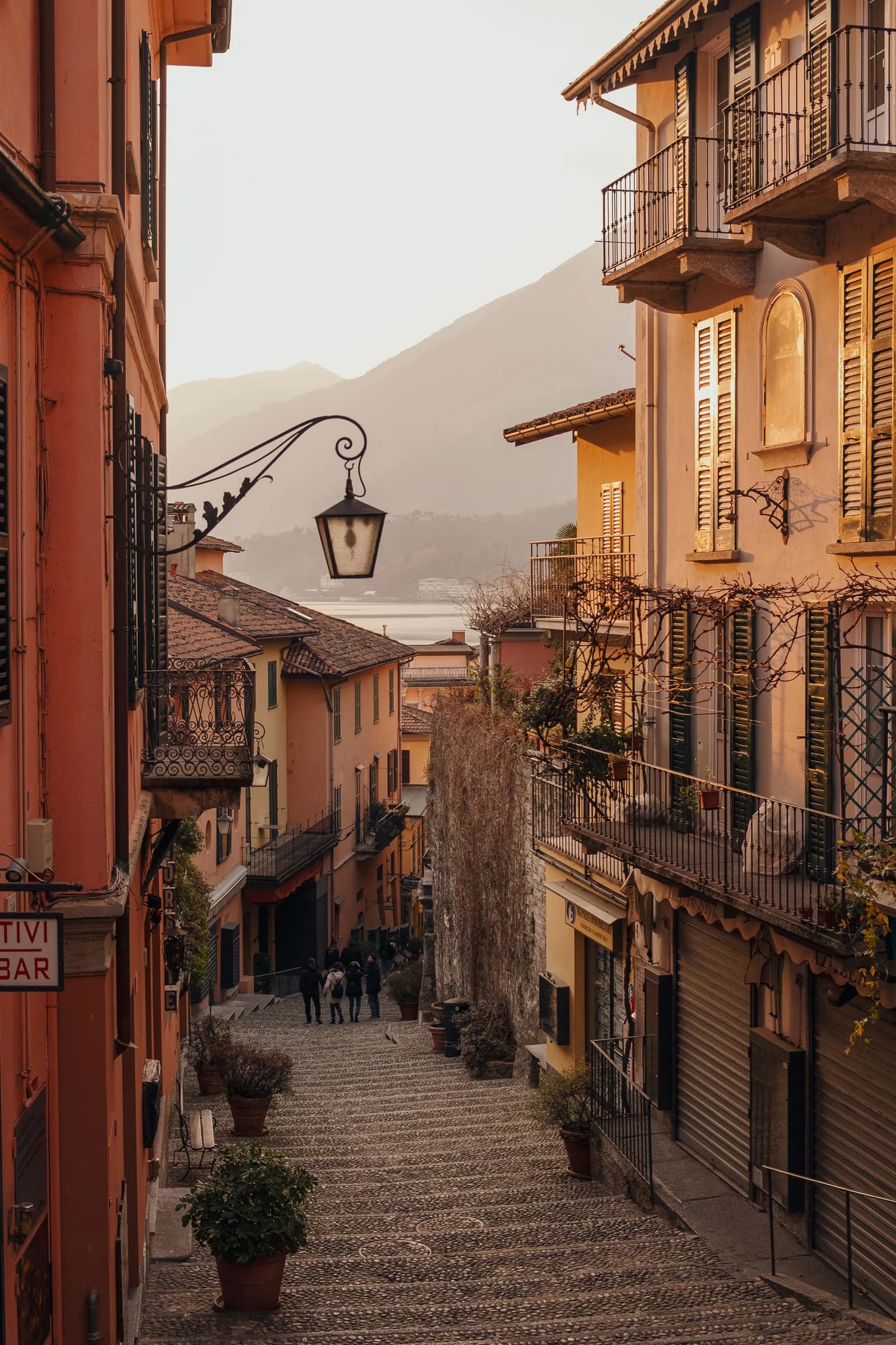 Stepped Italian lake town alley with ochre houses and mountain visible at end