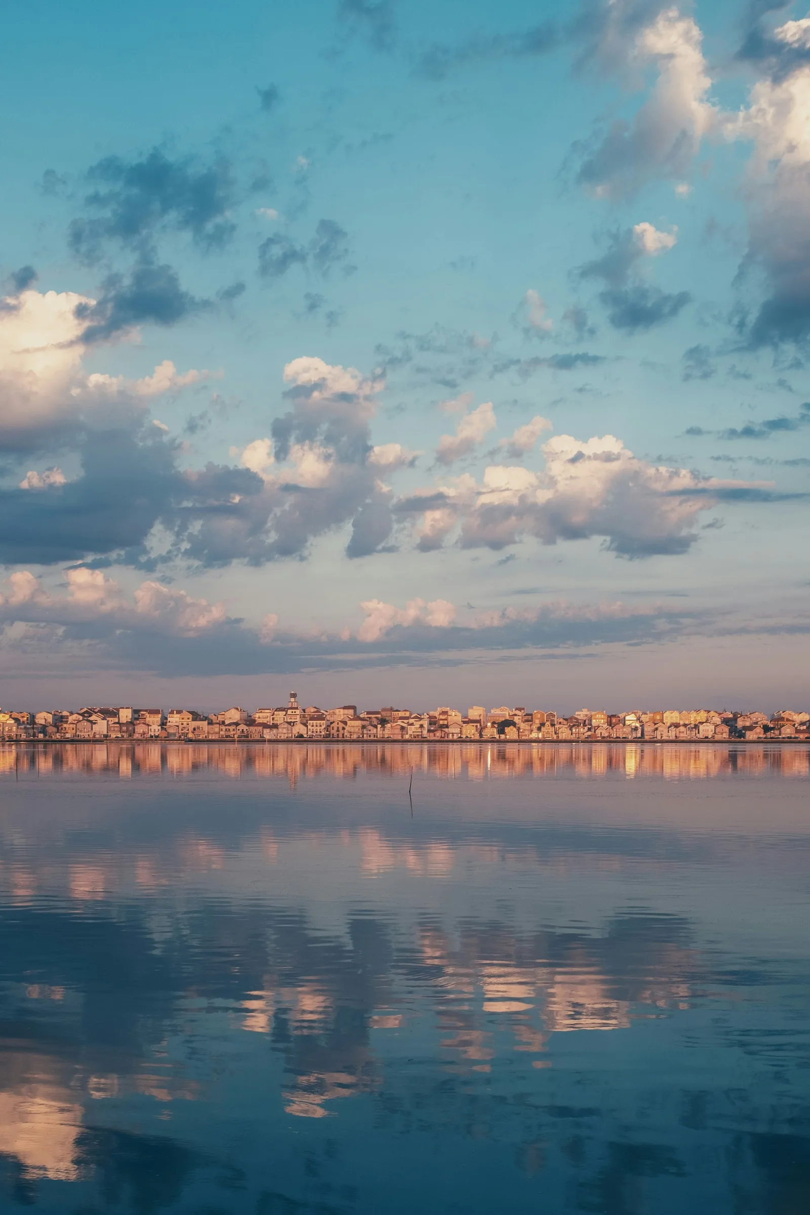 Town reflected on still water under a wide cloud-streaked sky